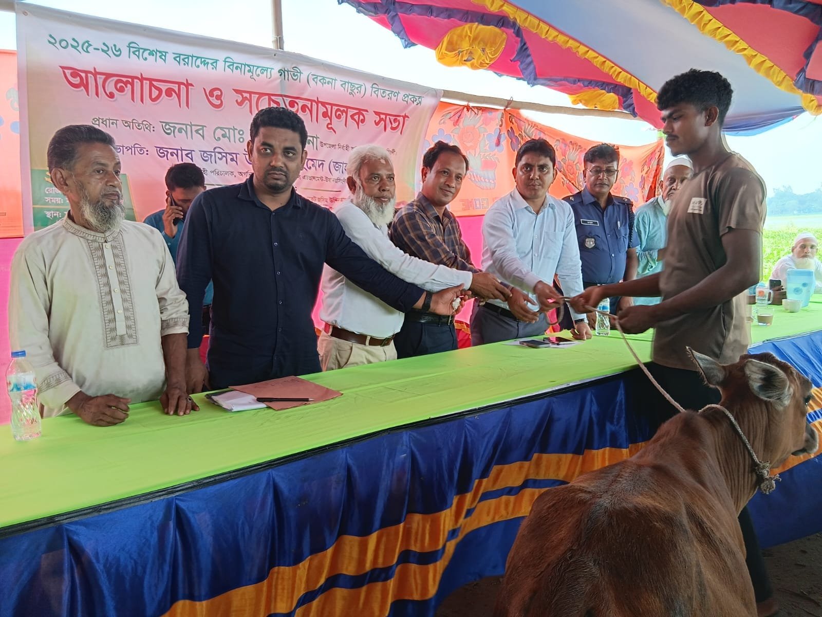 Officials handing the rope of a brown cow across the panel table to a young beneficiary.